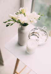 Bouquet of white freesias in vase and aromatic candle on table