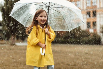 Waist up portrait of smiling little girl standing on grass and holding umbrella in hands. She is...