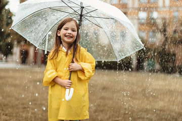Waist up portrait of smiling child spending time outdoors. She is standing with umbrella in hands...