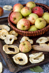 Dessert. Dried apple rings on an old baking sheet, next to a wicker brown basket with fresh ripe apples. 