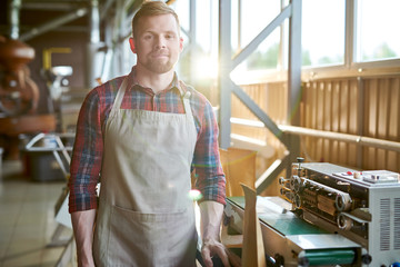 Fototapeta premium Sunlit waist up portrait of smiling bearded man wearing apron posing in artisan coffee roastery, copy space