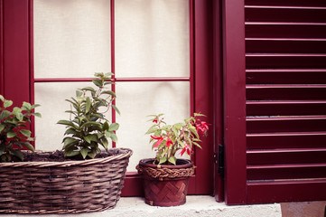 Cozy house with red wooden shutters and pots with flowers on windows