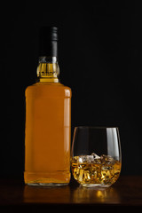 Glass of whiskey and it's bottle with dark background