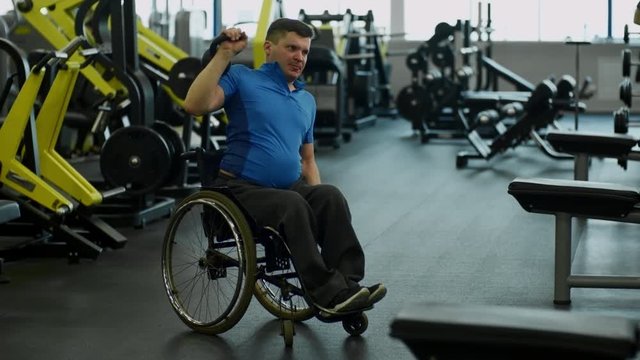 Tilt up of determined paraplegic man in wheelchair doing kettlebell shoulder press exercise in gym