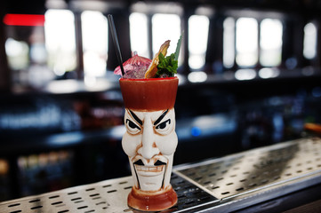 Alcoholic cocktail with mint and lime in originally voodoo earthen glass on bar table.