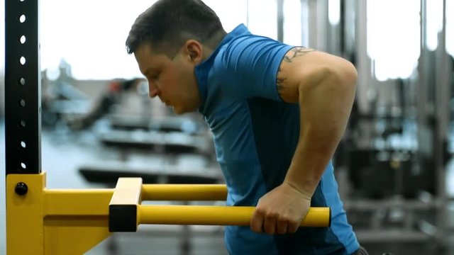 Tilt up of disabled man in wheelchair doing dips in gym