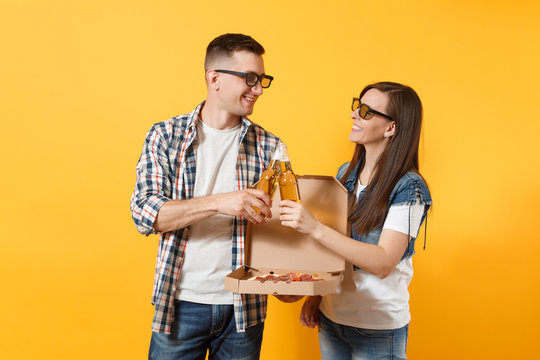 Young couple woman man sport fans in 3d glasses cheer up support team clinking beer bottles holding italian pizza in cardboard flatbox isolated on yellow background. Sport family leisure lifestyle.