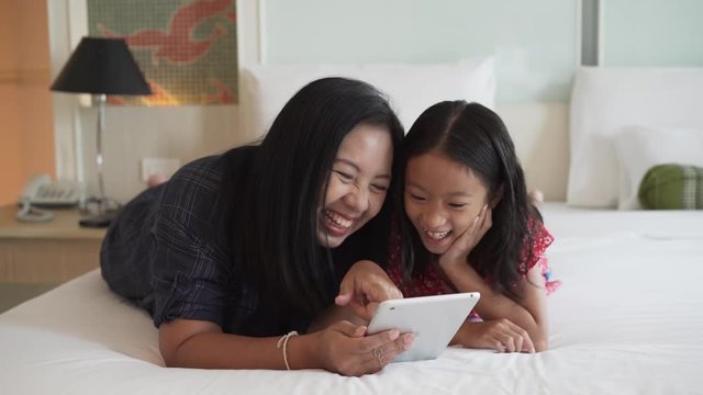 Mother and daughter enjoy playing computer tablet on the bed