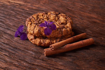 watered chocolate syrup cookies on wooden table. Cute composition with flowers and sticks of cinnamon. Selective focus