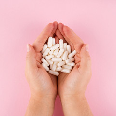 Hands hold pills isolated on pastel coloured background. Medication and prescription pills flat lay background.