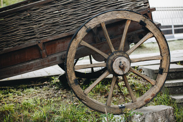 wooden cart wheel on an old wicker cart on the grass.