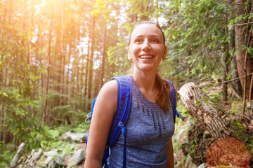 Young smiling woman with backpack hiking in mountain forest