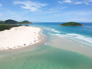  Aerial view of Brazilian beach with blue sky, white clouds, tourists in the sand, green and blue sea.