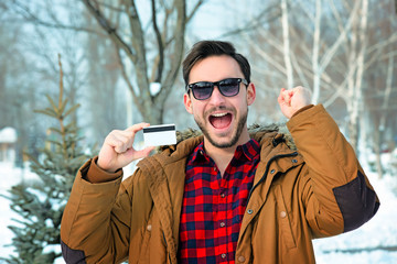 Happy handsome guy in a sunglasses is holding a credit card. Beautiful man with a beard looks like a winner. Rich and satisfied male