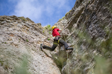 Photo from back of climbing young sports guy in yellow helmet on rock at summer day