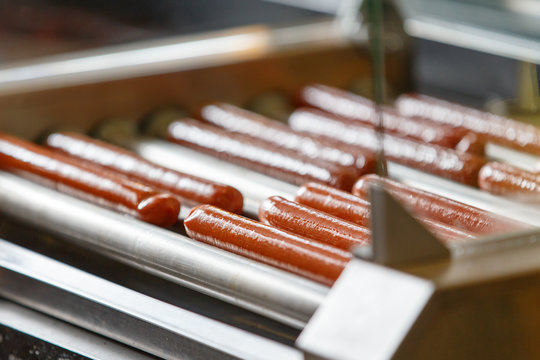 Greasy Hot Dog Sausages On Turning Cooking Machine In Cafe