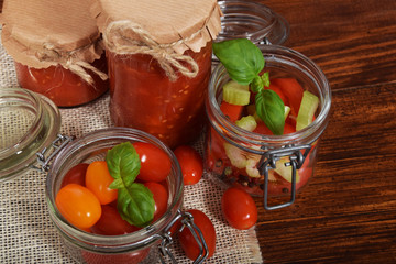 jar with tomato sauce for the winter, cherry tomatoes, garlic, spices, colorful pumpkins and scattered kitchen salt, mortar for the winter