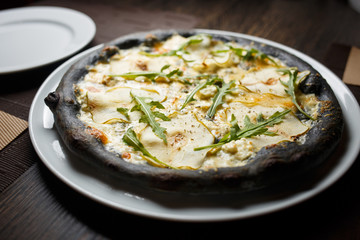 Black four cheese pizza served on the table in restaurant. Quattro formaggi pizza with pears on black dough