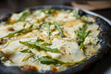 Black four cheese pizza served on the table in restaurant. Quattro formaggi pizza with pears on black dough