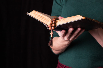 Rosary, cross and Bible  in female hands on a dark background. Holy book.