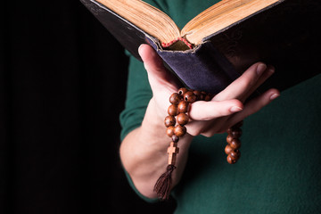Rosary, cross and Bible  in female hands on a dark background. Holy book.