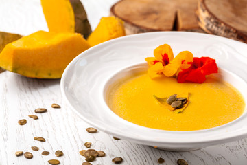 Ukrainian cuisine. Pumpkin puree soup, with cream, pumpkin seeds and flowers on a white plate. Copy space, selective focus
