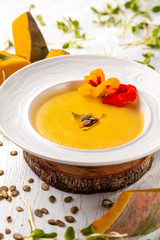 Ukrainian cuisine. Pumpkin puree soup, with cream, pumpkin seeds and flowers on a white plate. Copy space, selective focus