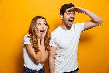 Image of delighted man and woman 20s in basic clothing screaming in surprise and looking aside with hand at forehead, isolated over yellow background