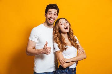 Portrait of cheerful people man and woman in basic clothing smiling and showing thumb up at camera,...