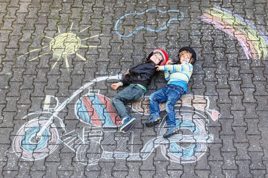 Creative leisure for children: two little funny friends in helmet having fun with motorcycle picture drawing with colorful chalks. Children, lifestyle, fun concept