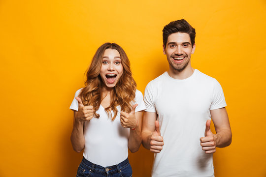 Image of happy young people man and woman in basic clothing laughing and showing thumbs up at camera, isolated over yellow background