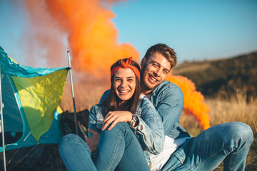 Young happy couple holding smoke bombs on camping