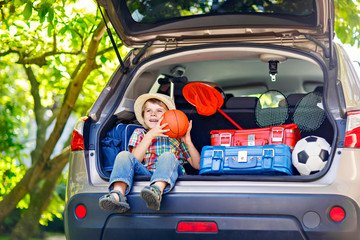 Little kid boy sitting in car trunk just before leaving for vaca
