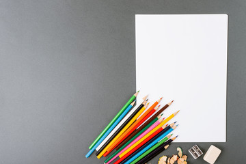 Color pencils on a gray background with a white sheet ready for drawing
