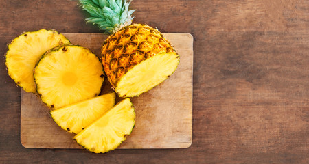 Pineapple on wood texture background. Whole and sliced tropical pineapple on wooden cutting board  with copy space. Top view.