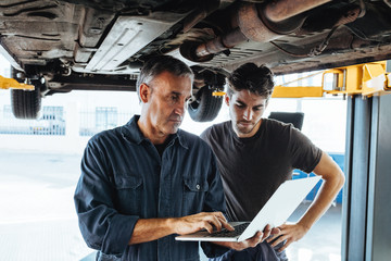 Mechanics using laptop while examining the car