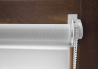 Details of white fabric roller blinds on the plastic window with wood texture in the living room.