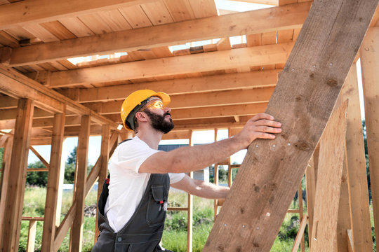 The man is a builder on the roof of a wooden frame house.