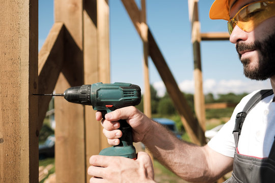 The man is a builder on the roof of a wooden frame house.