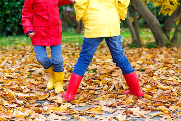Closeup of kids legs in rubber boots dancing and walking through fall leaves