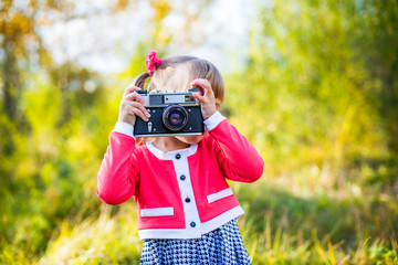 a little girl in a pink jacket and a black and white dress with two tails photographing an old camera