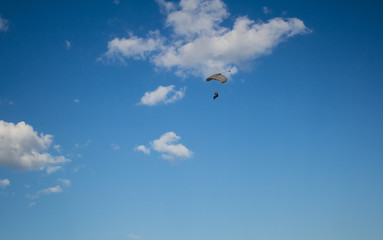 Naklejka na ściany i meble Man, a paratrooper is flying through the blue sky amidst white clouds on a parachute