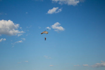 Man, a paratrooper is flying through the blue sky amidst white clouds on a parachute
