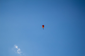 Man, a paratrooper is flying through the blue sky amidst white clouds on a parachute