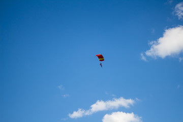 Man, a paratrooper is flying through the blue sky amidst white clouds on a parachute