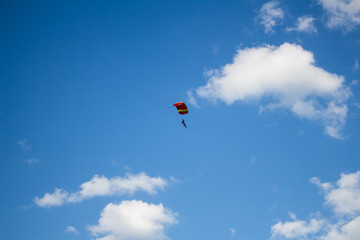 Man, a paratrooper is flying through the blue sky amidst white clouds on a parachute