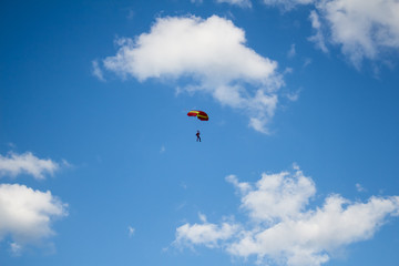 Man, a paratrooper is flying through the blue sky amidst white clouds on a parachute