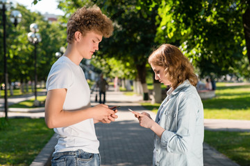 The boy and girl are facing each other. Summer in nature. In his hands holds a smartphone. Emotion dating in the park. The concept of dating in nature. The guy gets acquainted with the girl.