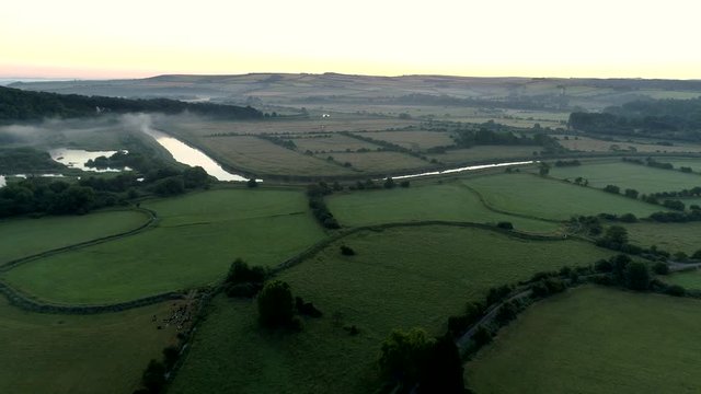 Drone flies slowly over a misty predawn English landscape in West Sussex near the River Arun
