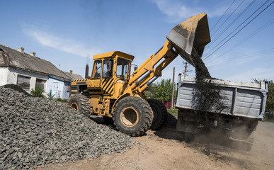 Yellow loader delivering stone gravel into truck during road construction works. The stones for the...